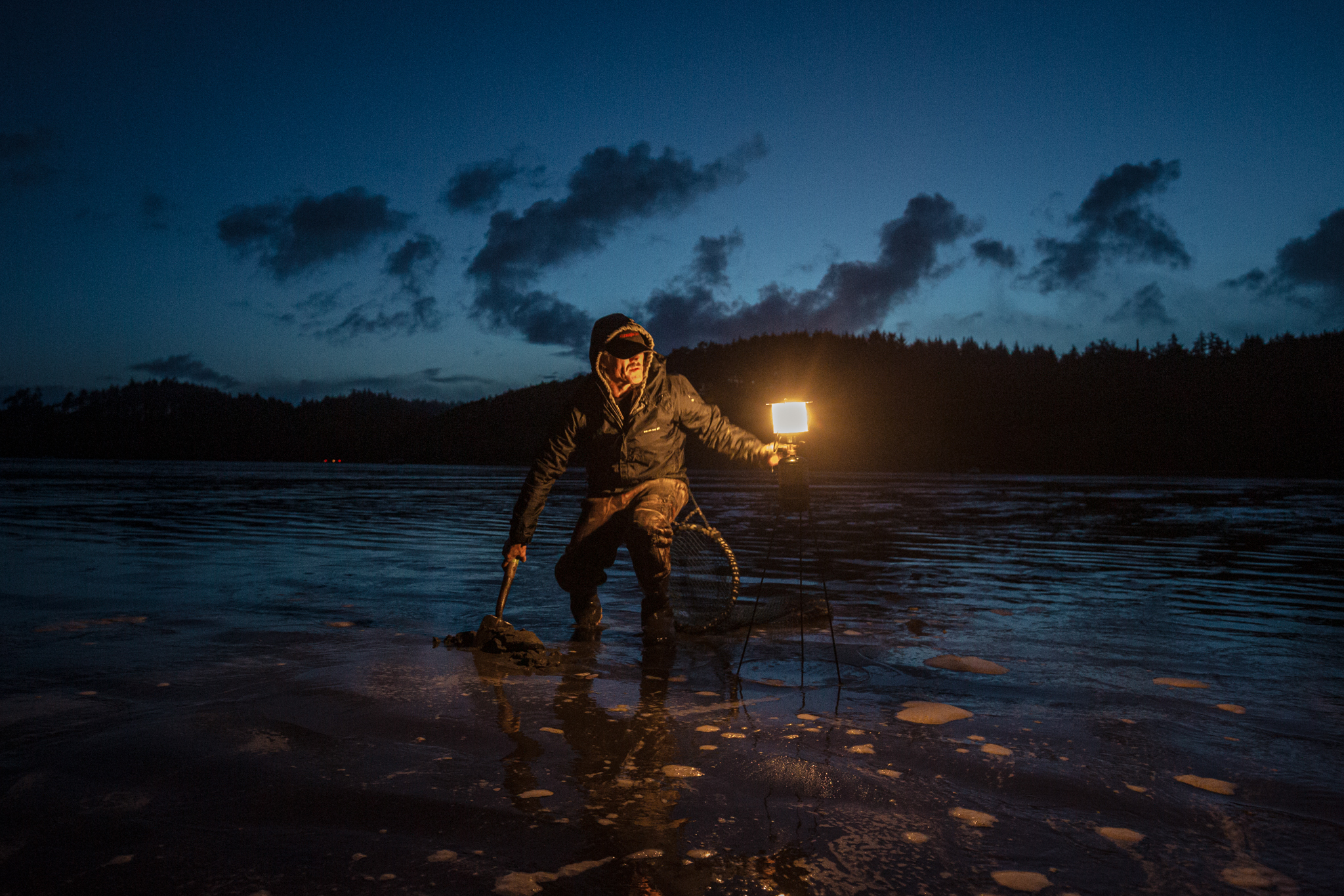 At night, and lit by a handheld light, a man digs for razor clams.