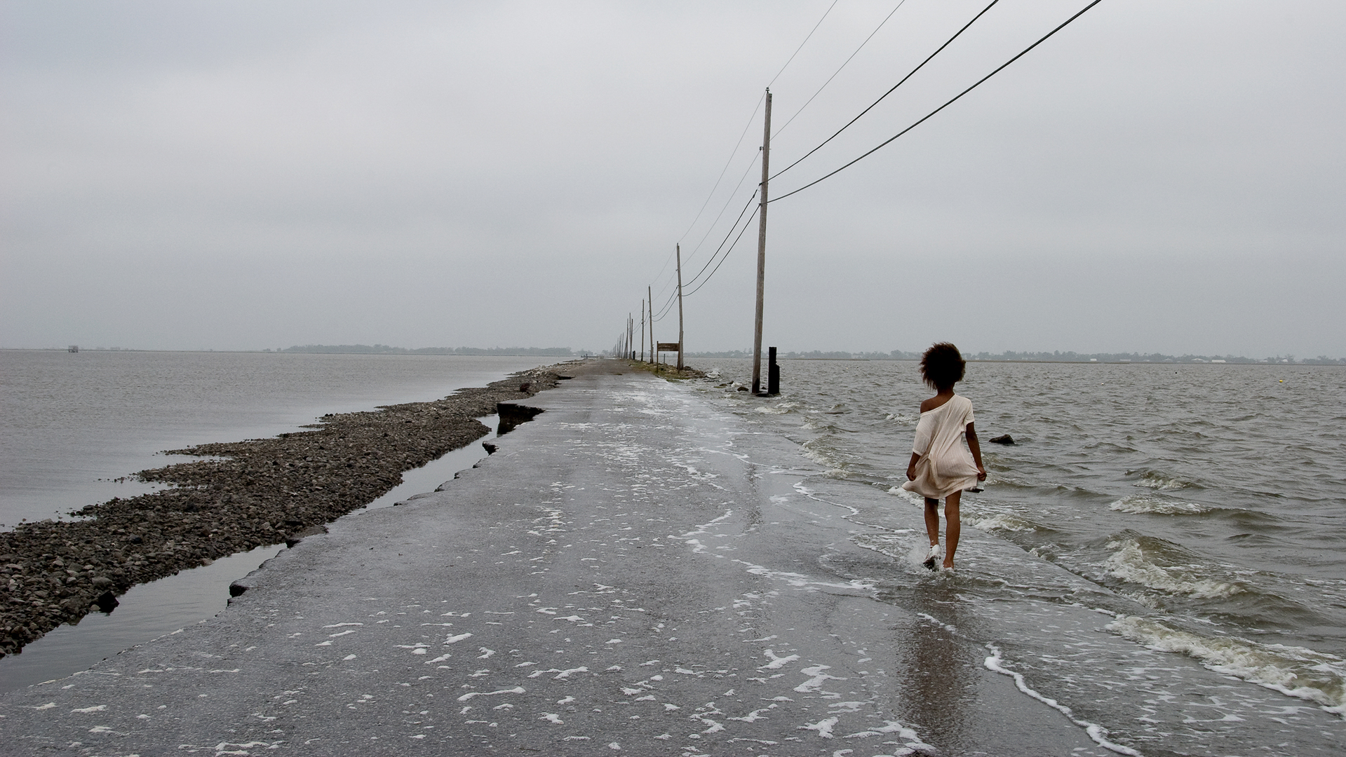 A person walks down a flooded and eroded road during a tropical storm.